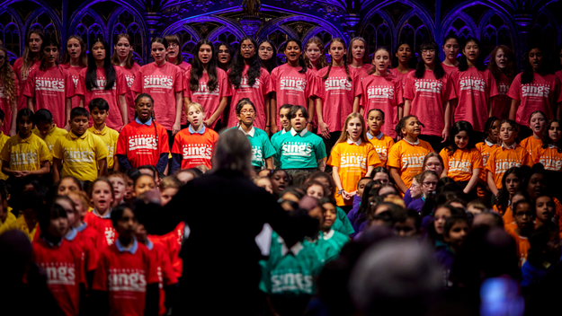 A massed choir of children perform in colourful t-shirts of rainbow hues at Manchester Cathedral